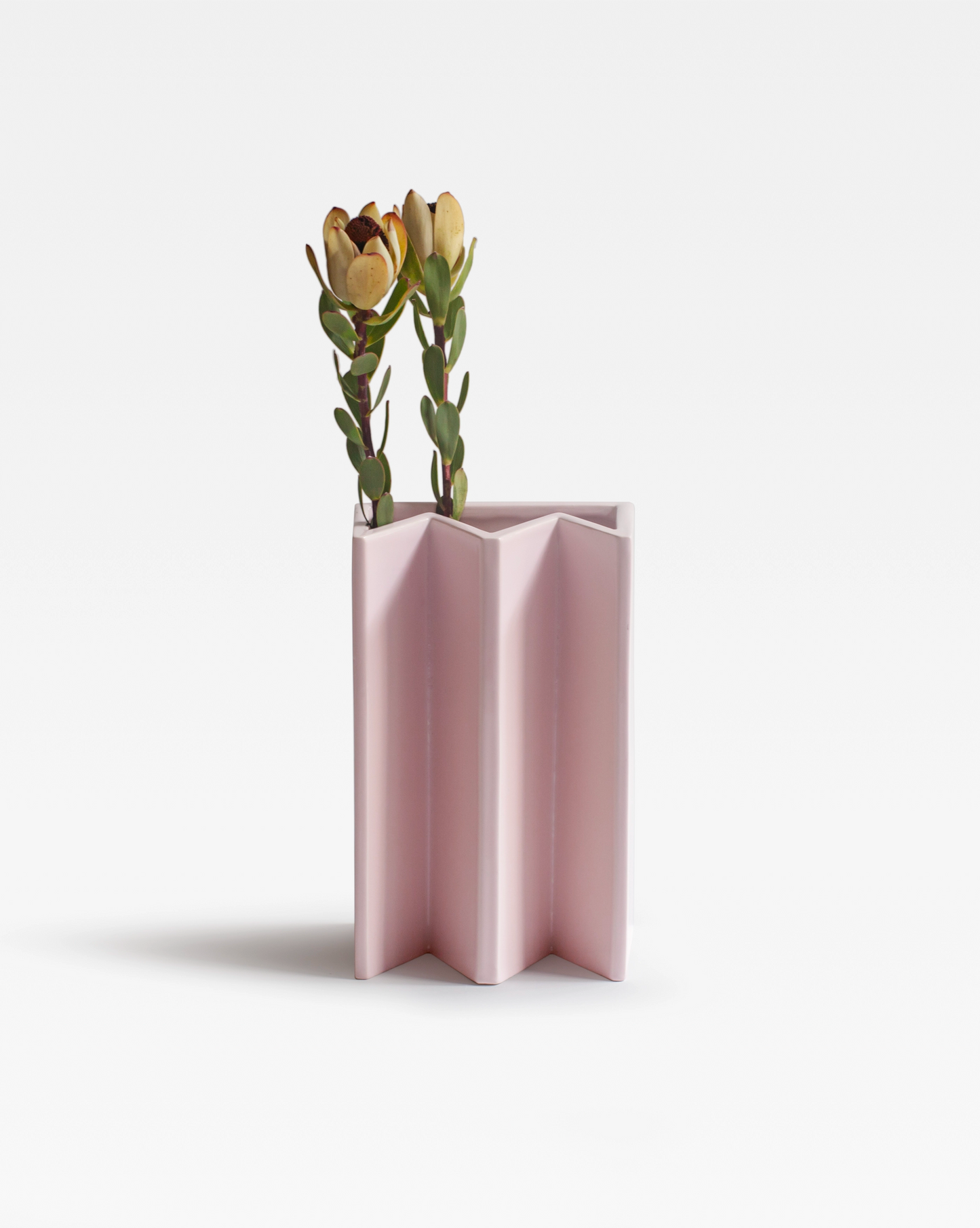 Geometric design of the Pink King Vase, showcasing its sculptural form in vibrant pink ceramic and two yellow flowers.