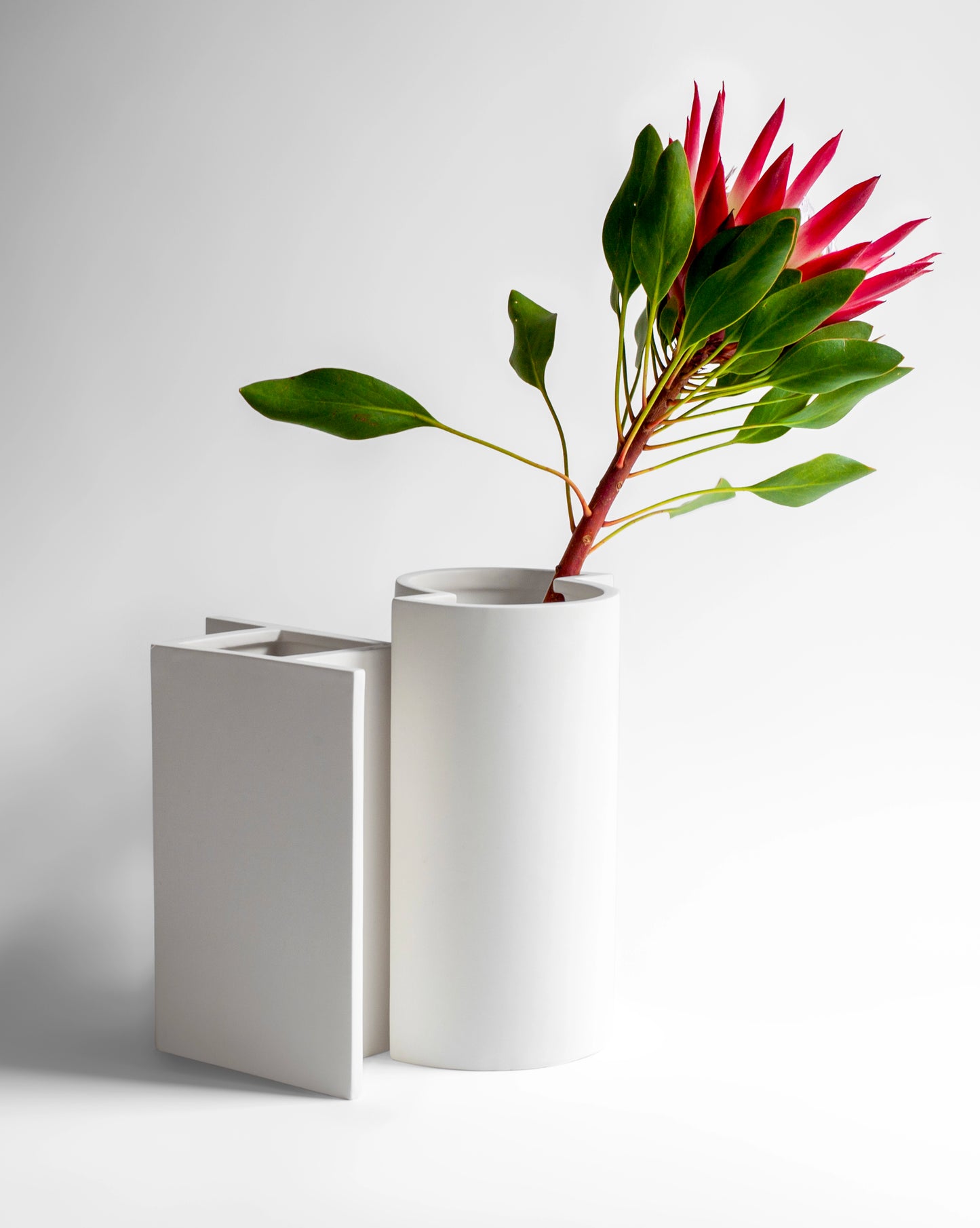 Modern matte white geometric ceramic vases with a sophisticated design and pink flower.