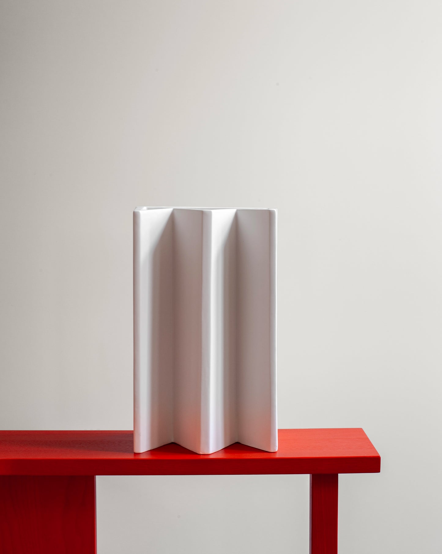 Sleek and minimalist white King Vase with a matte texture from the Kish o Mat collection on a red Grcic armchair.